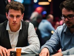 Dvojica muškaraca za poker stolom — jedan nosi belu košulju i prsluk, drugi nao?are, obojica pažljivo upravljaju svojim žetonima