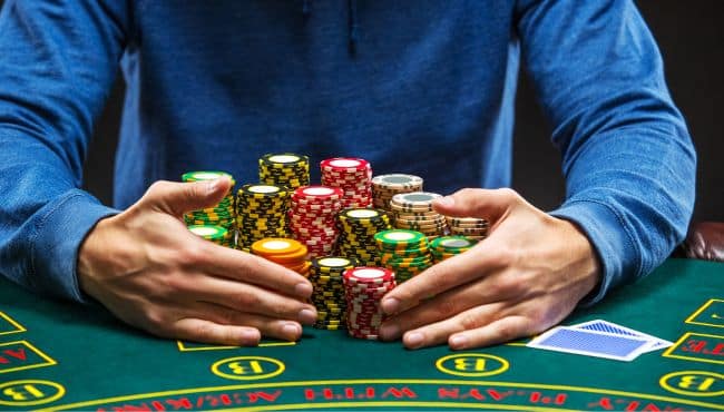 Igra? u plavoj dukserici obuhvata veliku gomilu šarenih žetona na stolu, naglašavaju?i veli?inu uloga