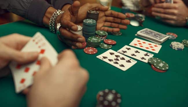 Ruke igra?a i šareni žetoni na zelenom poker stolu, dok otkrivene karte odlu?uju ishod partije