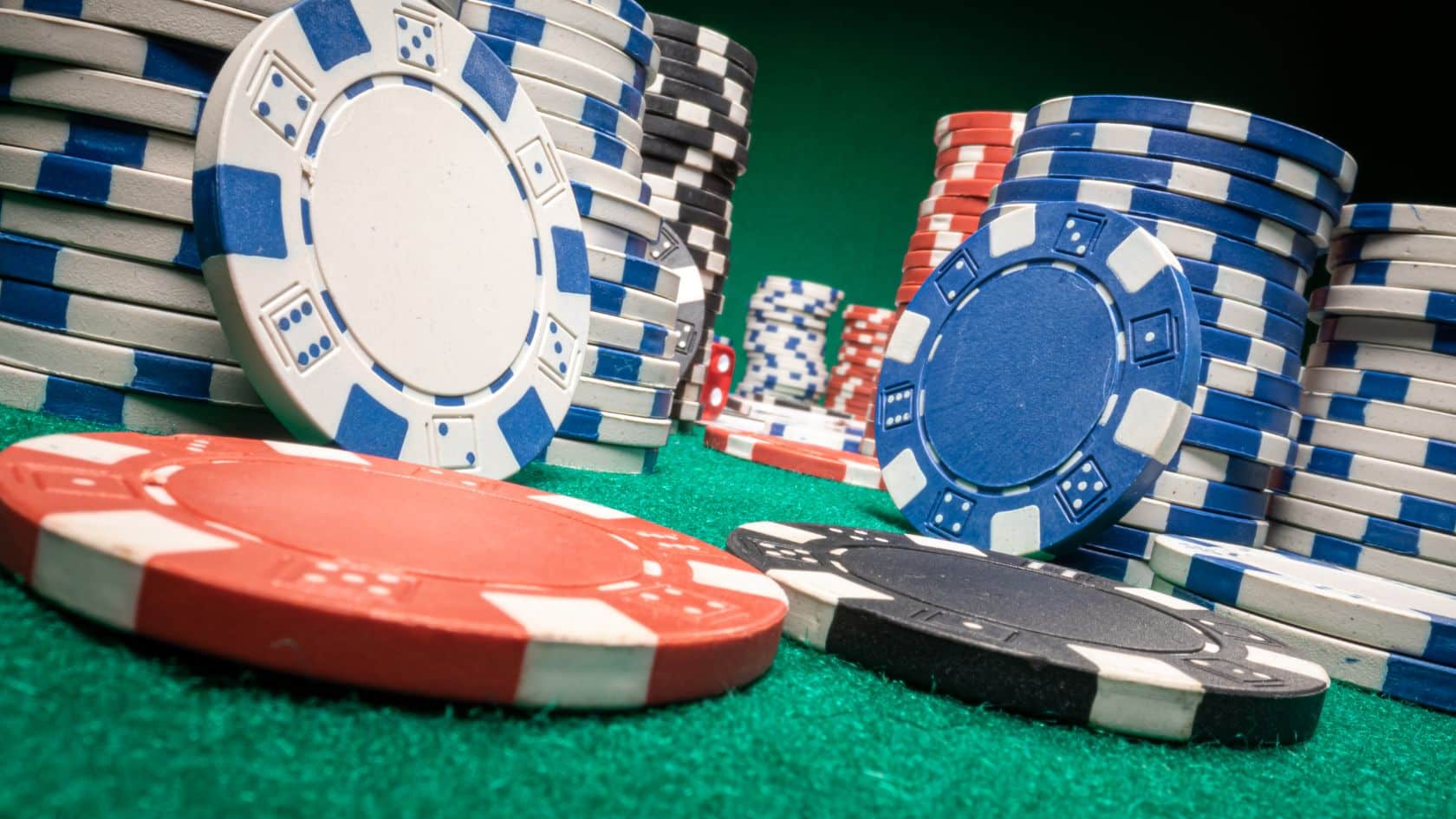 Pove?a koli?ina poker ?ipova u razli?itim bojama pore?anih na zelenom stolu, spremnih za igru.