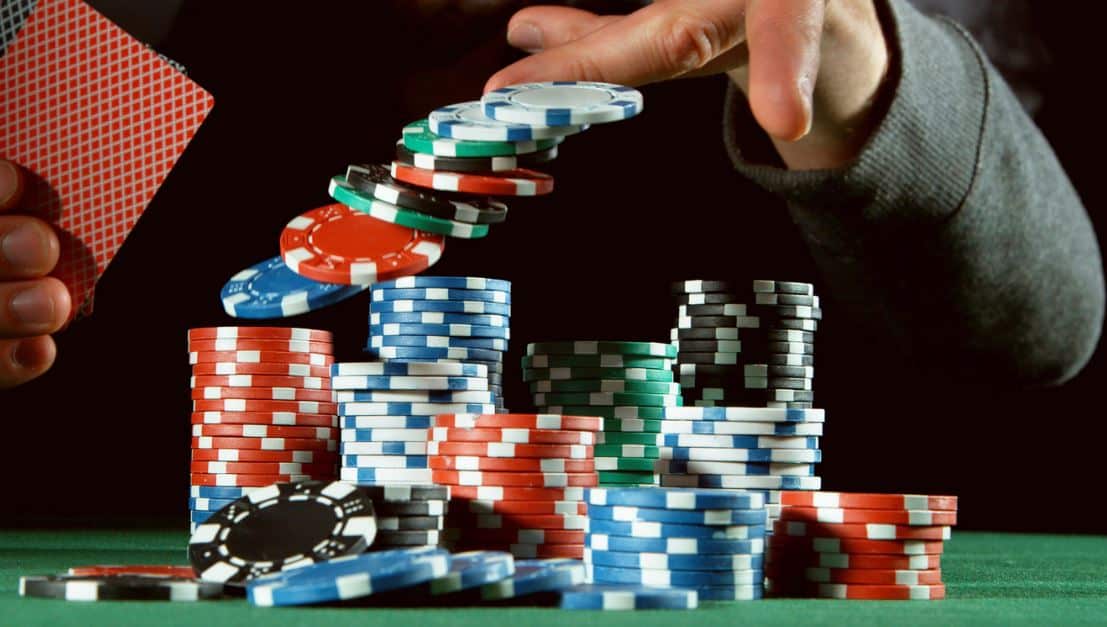 Ruka koja baca šarene žetone u vazduh iznad uredno složenih gomila, dok druga ruka drži karte