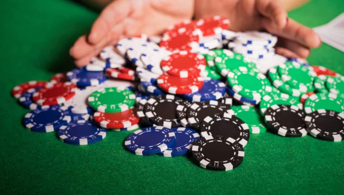 Ruka koja grabi hrpu raznobojnih poker žetona na zelenom stolu, naglašavaju?i all-in potez