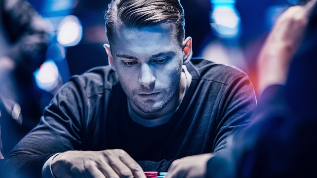 Muškarac u svedenom, plavi?nom osvetljenju fokusirano razmešta žetone tokom partije pokera