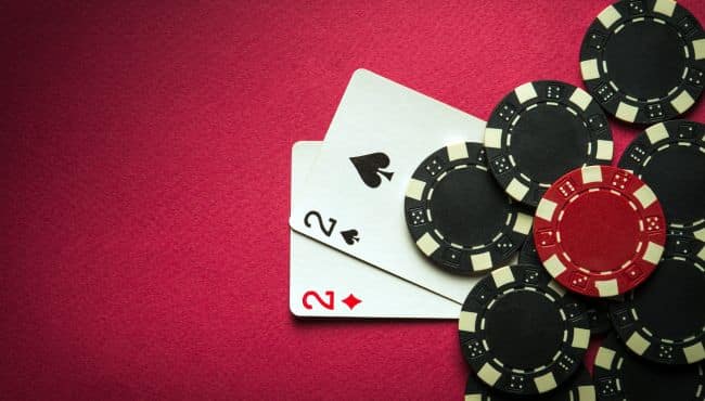 Par dvojki – pik i karo – okružen crnim poker žetonima na crvenoj podlozi.