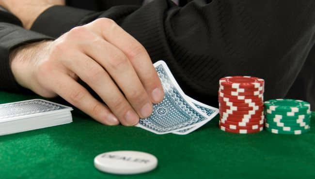  Igra? u odelu diskretno podiže karte za stolom sa zelenom poker platnom.