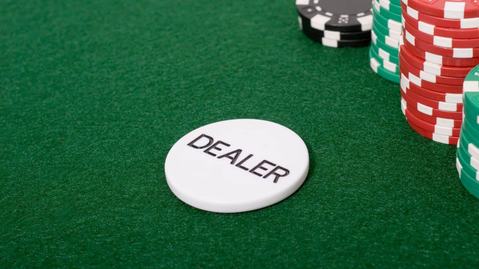 Beli dugme sa natpisom "DEALER" na poker stolu okruženom žetonima.
