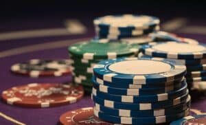 Naslagani plavo-zeleni poker žetoni na ljubičastoj podlozi, ističući visinu uloga u igri