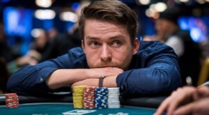 Muškarac oslonjen na ruke, zamišljeno gleda preko gomile šarenih poker žetona, reflektujući napetu atmosferu igre