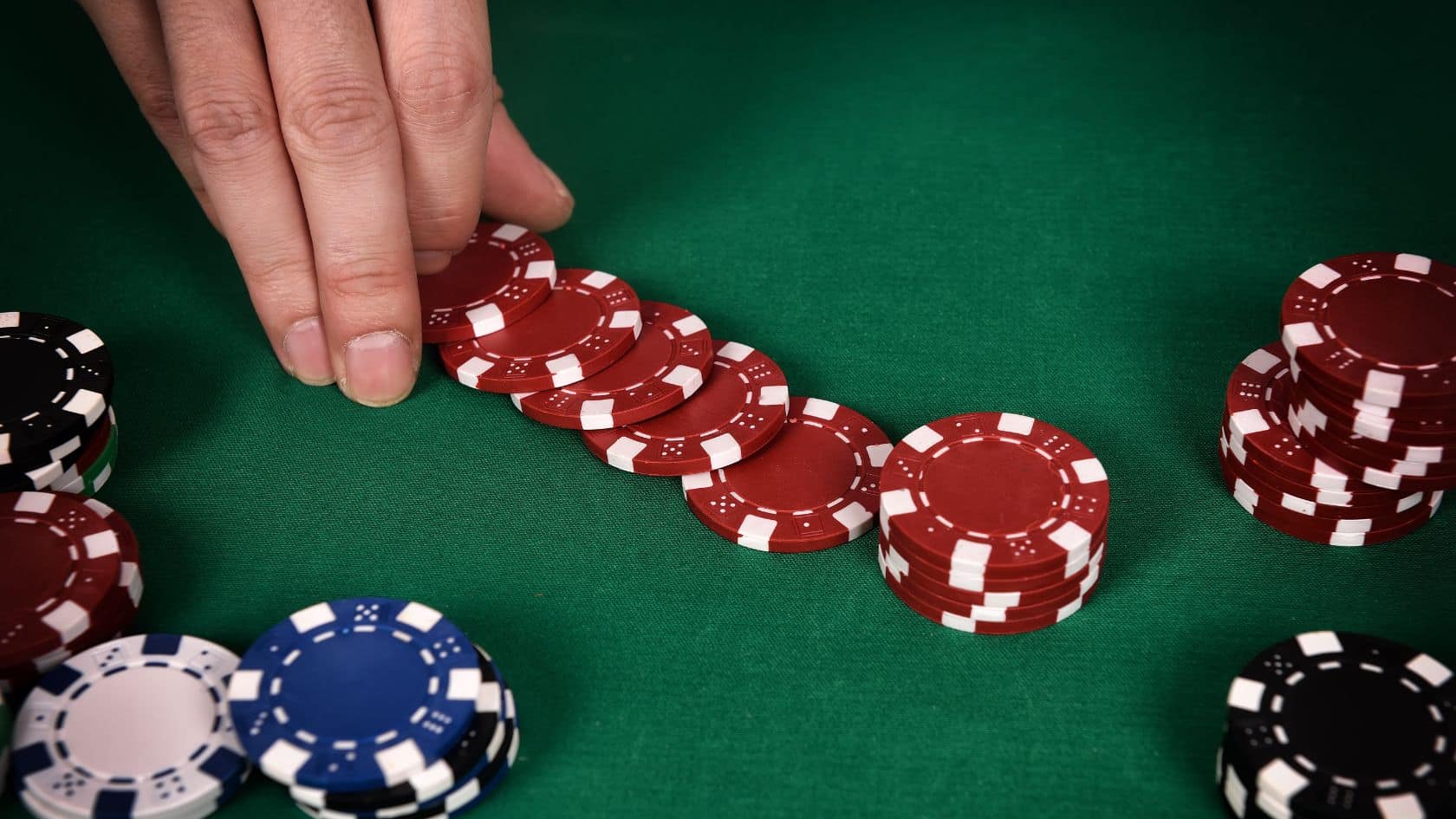 Ruka igrača pomera niz crvenih žetona na zelenom poker stolu.