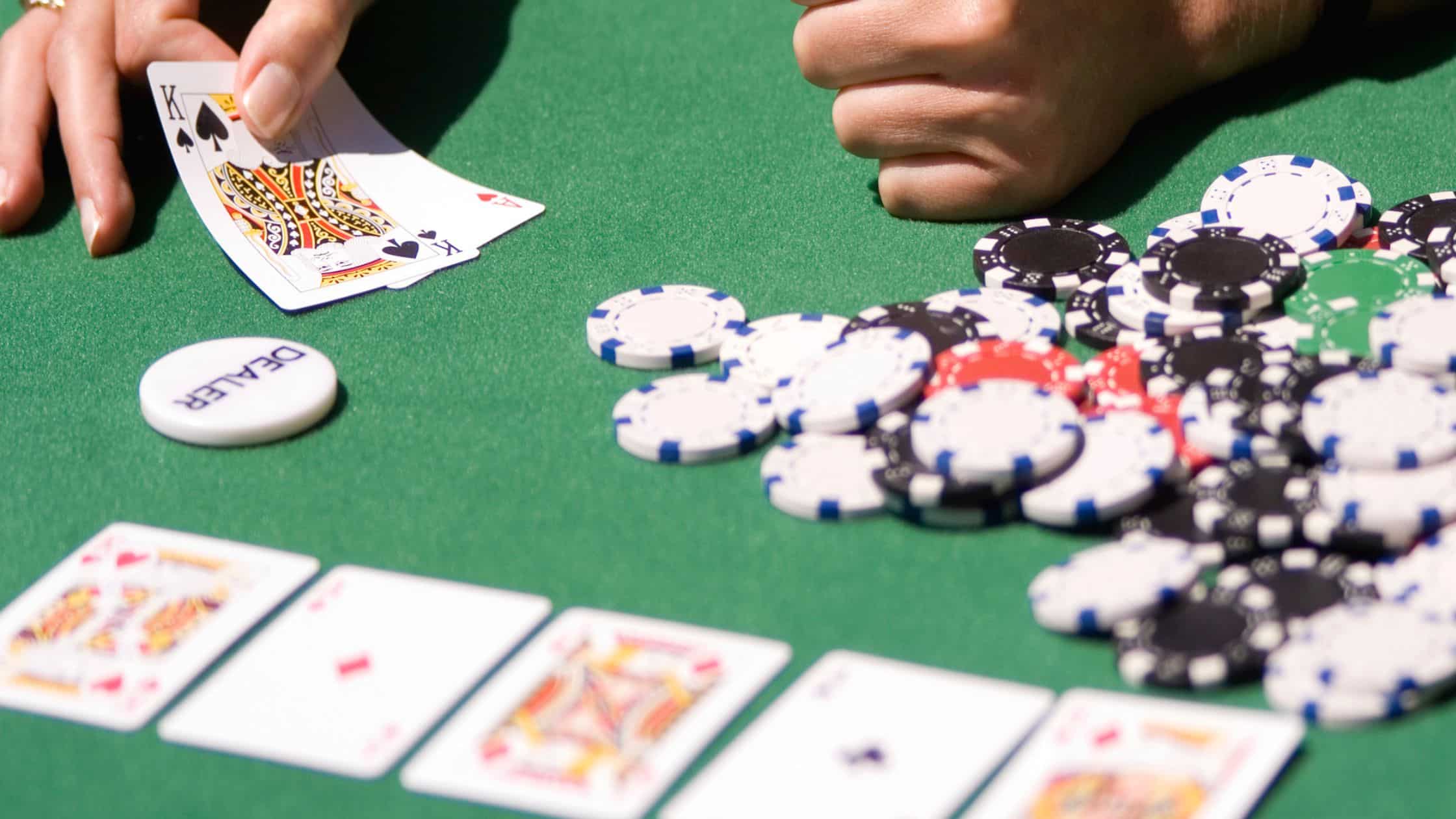 Igrač pokazuje ruku sa Kraljem pik i Asom herc pored gomile poker žetona.