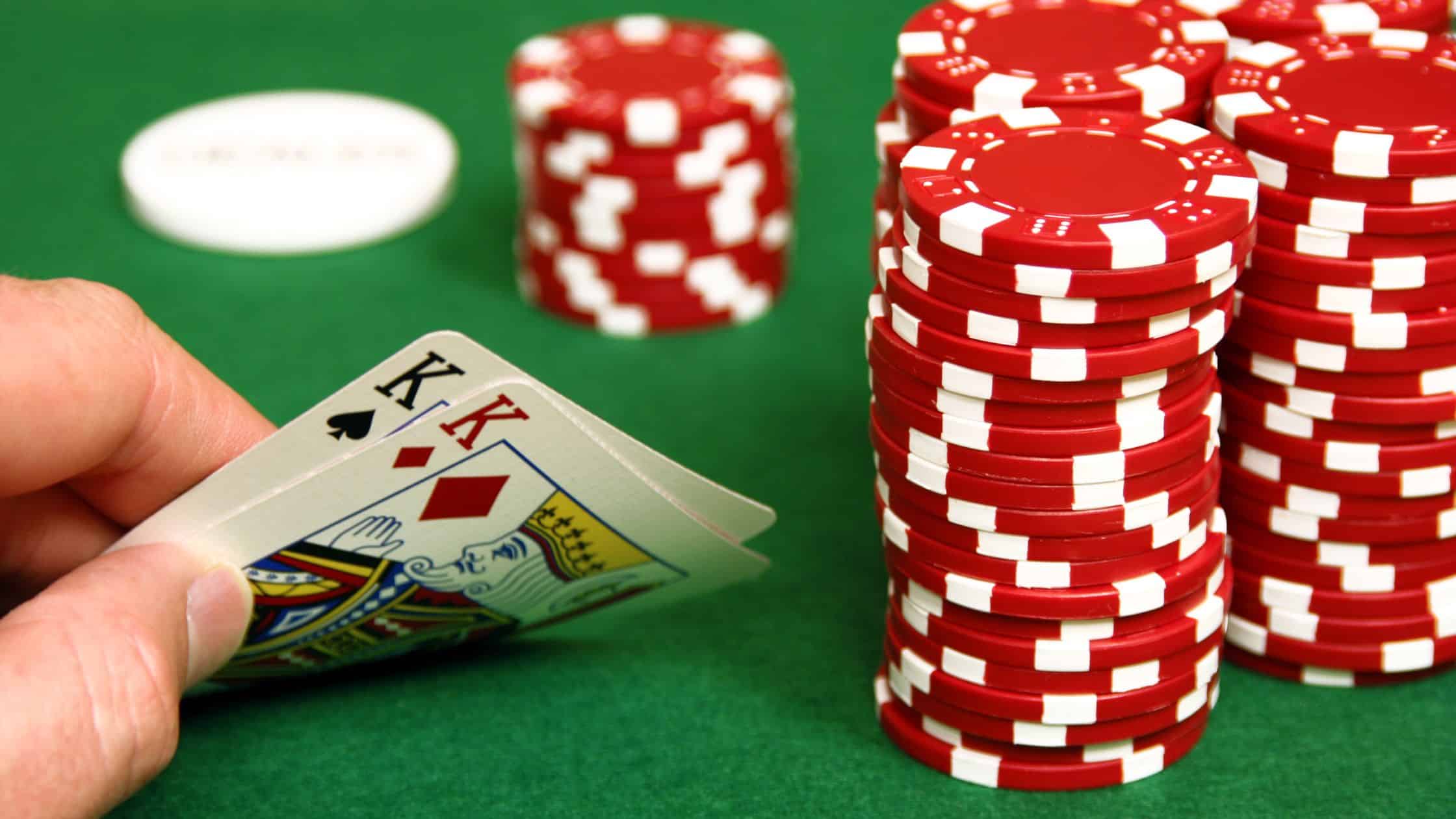 Igrač drži par kraljeva u ruci pored visokih gomila crvenih poker žetona.