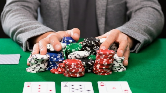 Ruke i žetoni na stolu, igrač gura sve žetone „all-in“ u partiji pokera