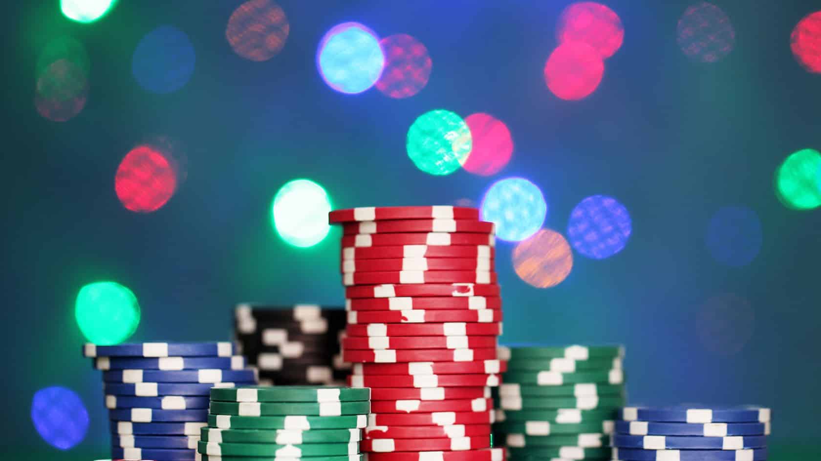 Visoke naslagane gomile poker žetona u različitim bojama sa svetlima u pozadini.