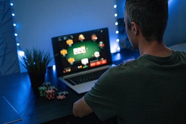 vīrietis spēlē pokeru uz klēpjdatora ar žetoniem blakus tastatūrai